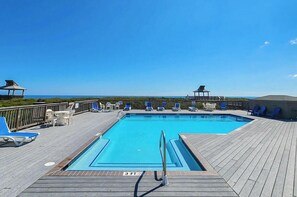 Ein Pool mit Holzterrasse, Liegestühlen und Blick auf den Ozean.