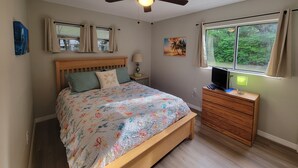 A bedroom with a bed, a ceiling fan, a window with a view of greenery, a nightstand with a lamp, and a dresser. - 3 Bed/2 Bath Cottage near downtown  Crystal River (Crystal River)