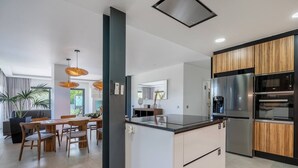 A modern kitchen with a central island, built-in ovens, and a dining area with a large window. - Stylish Algarve Retreat- Priv. Pool & Beach Nearby (Quarteira)