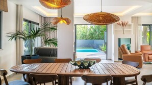 A modern dining area with a wooden table and chairs, surrounded by large windows and a view of a swimming pool. - Stylish Algarve Retreat- Priv. Pool & Beach Nearby (Quarteira)