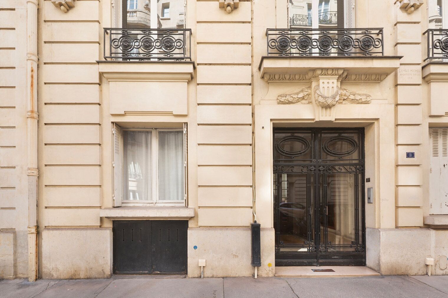 A building facade with a large black door, a window with a curtain, and a balcony with ornate metal railings.