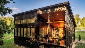 A modern wooden cabin with large windows, a deck, and a small garden area.