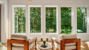 A room with large windows, two wooden chairs, a round coffee table, and a small plant.