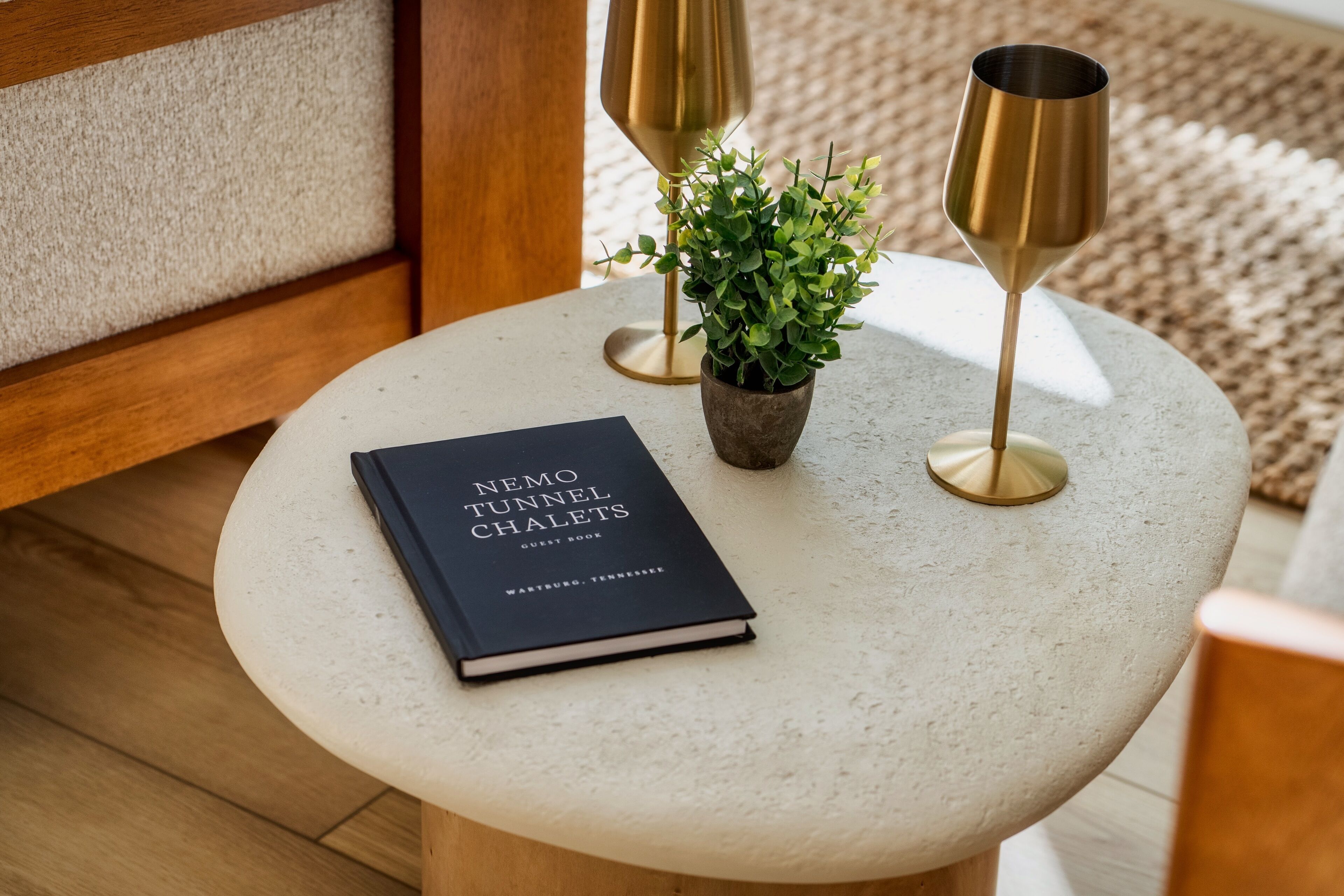 A round table with a book titled "Nemo Tunnel Chalets" and two gold-colored candle holders with a small potted plant.