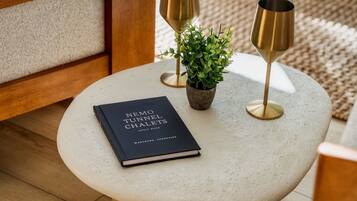A round table with a book titled "Nemo Tunnel Chalets" and two gold-colored candle holders with a small potted plant.