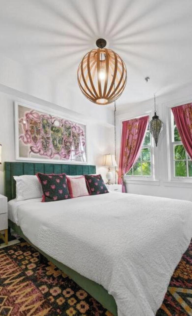 A bedroom with a large bed, a decorative ceiling light, a window with curtains, and a wall art piece.