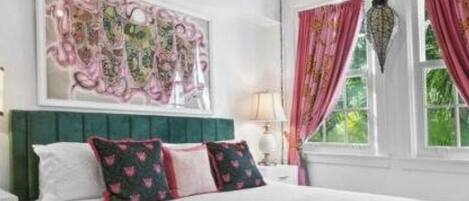A bedroom with a large bed, a decorative ceiling light, a window with curtains, and a wall art piece.