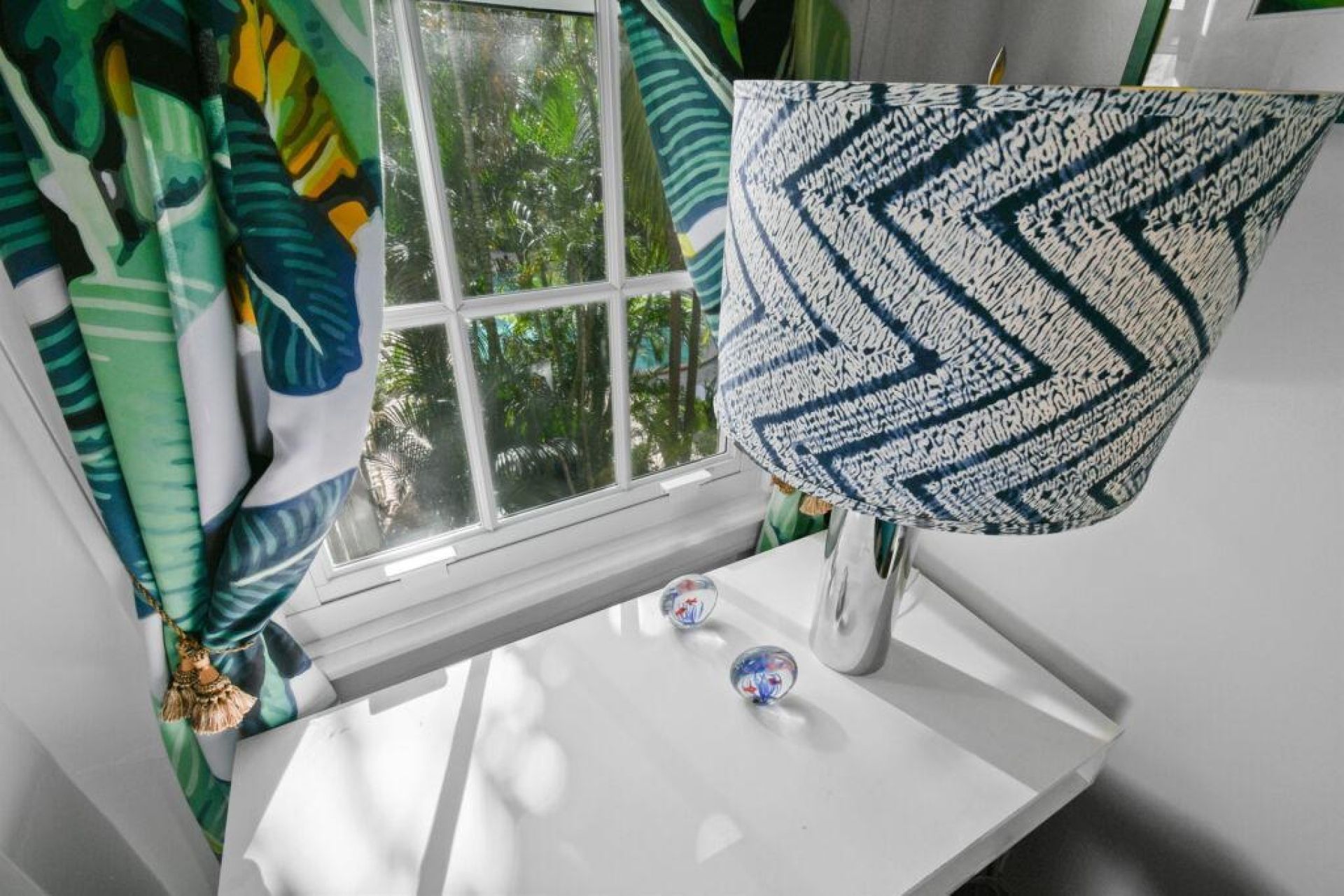 A room with a window, a white table, and a patterned cushion.