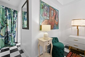 Quarto com piso xadrez, uma cadeira verde, cômoda branca e um quadro na parede.