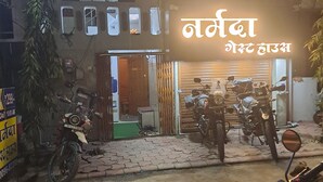 A building with a sign in a foreign language, a closed shop with motorcycles inside, and a motorcycle parked outside. - Narmada Guest House (Indore)