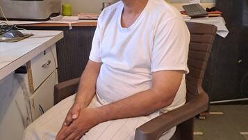 A man sitting in a chair in a room with a desk, drawers, a keyboard, and a mug.