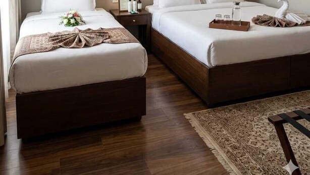 A hotel room with two beds, a ceiling fan, wall sconces, a wooden floor, and a rug. - Narmada Guest House (Indore)
