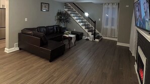 Ein Wohnzimmer mit einem dunkelbraunen Sofa, einem kleinen Tisch und einem Kamin. Eine Treppe führt zu einer weiteren Ebene.