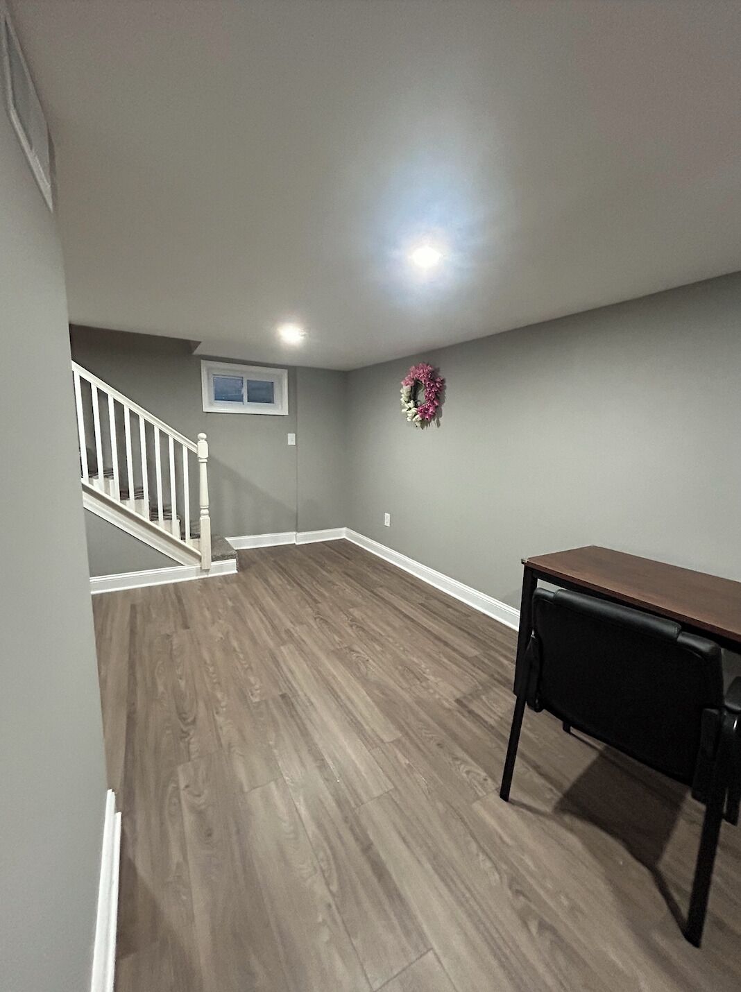 Una habitación amplia con piso de madera, barandal blanco, un ventanal pequeño y una guirnalda decorativa en la pared.