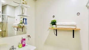 A bathroom with a white sink, mirror, and toilet. There are shelves with toiletries and a plant. - Room-modern Studio Hideaway Near City Sp (Iloilo)