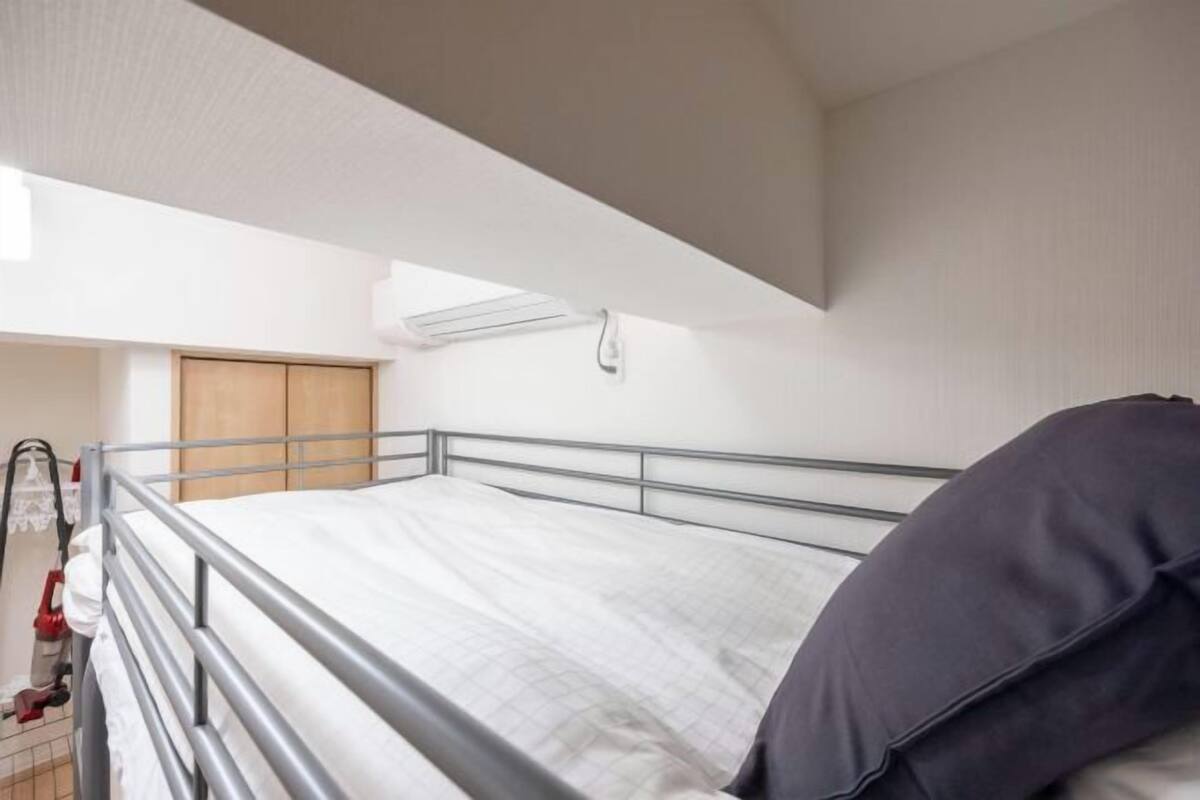 A bunk bed with a metal frame, a white mattress, and a dark-colored pillow.