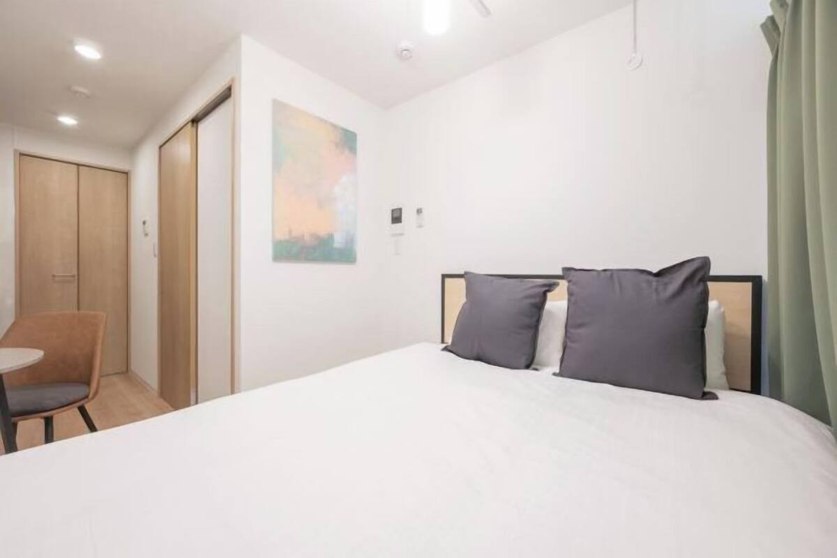 A hotel room with a bed, a chair, a desk, and a painting on the wall.