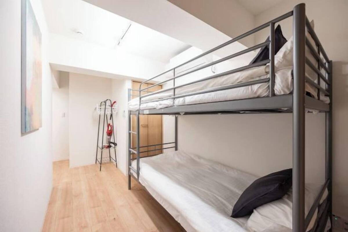 A bunk bed room with a wooden floor, a ladder, and a door leading to another room.