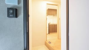 A hotel room with a wooden floor, a small bedside table, a bed with a wooden headboard, and a door leading to a bathroom. - MAT Nogata (Tokyo)