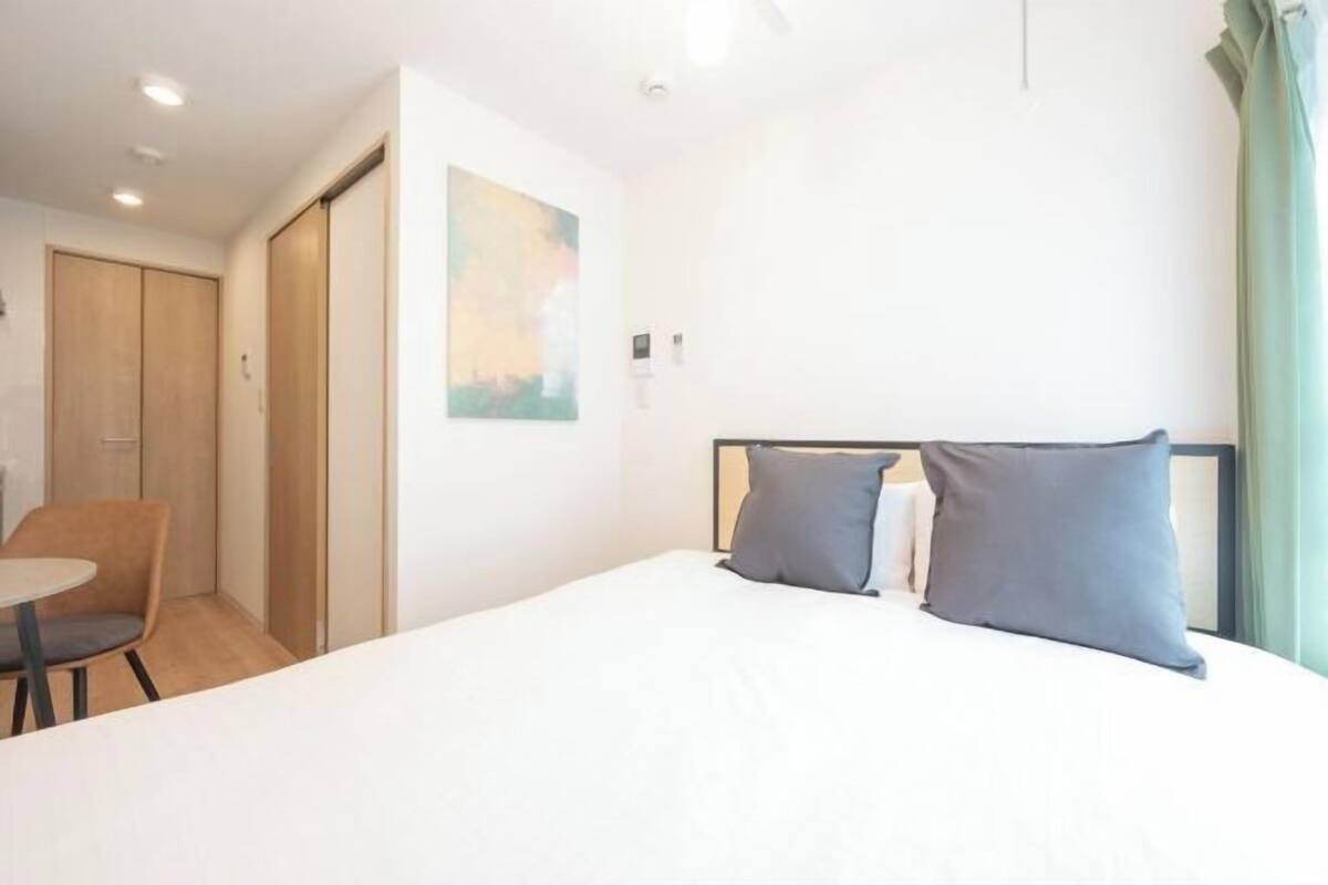 A hotel room with a bed, a chair, a desk, and a painting on the wall.