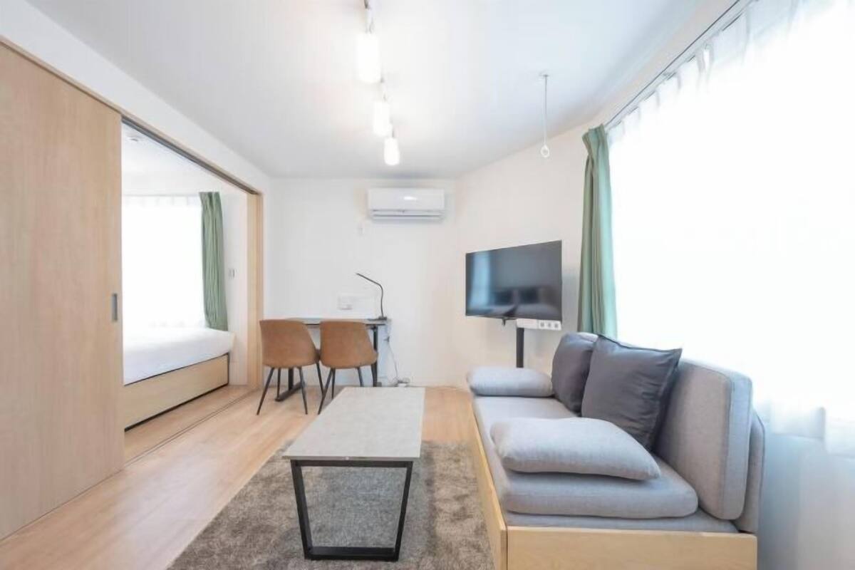 A modern living room with a sofa, a TV, a small table, and a desk with chairs.
