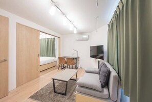A compact room with a bed, a sofa, a small table, a desk, and a TV. - MAT Nogata (Tokyo)