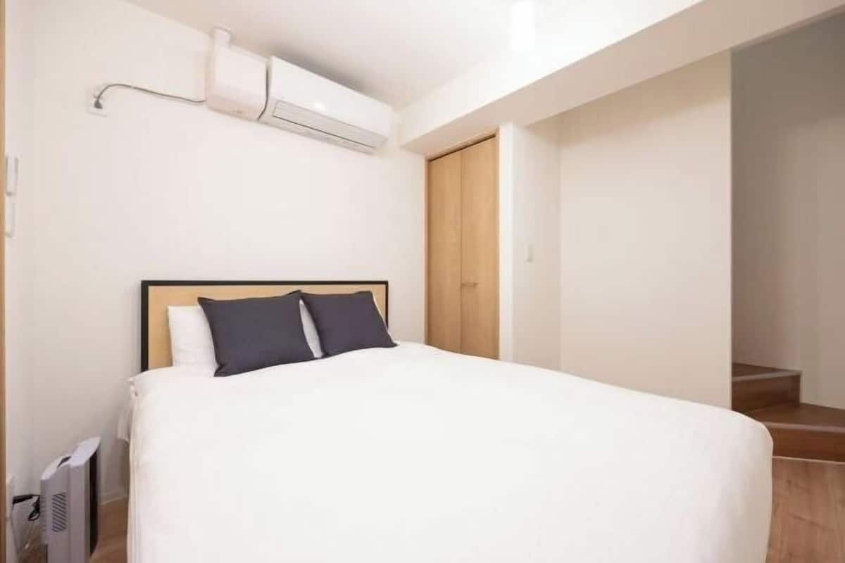 A hotel room with a bed, a wooden wardrobe, and an air conditioning unit.