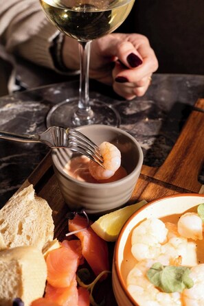 Une table à manger avec un saladier de crevettes, du pain et un verre de vin blanc.