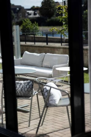 Un espace extérieur aménagé avec un canapé et des fauteuils, une table et une vue sur une rivière.