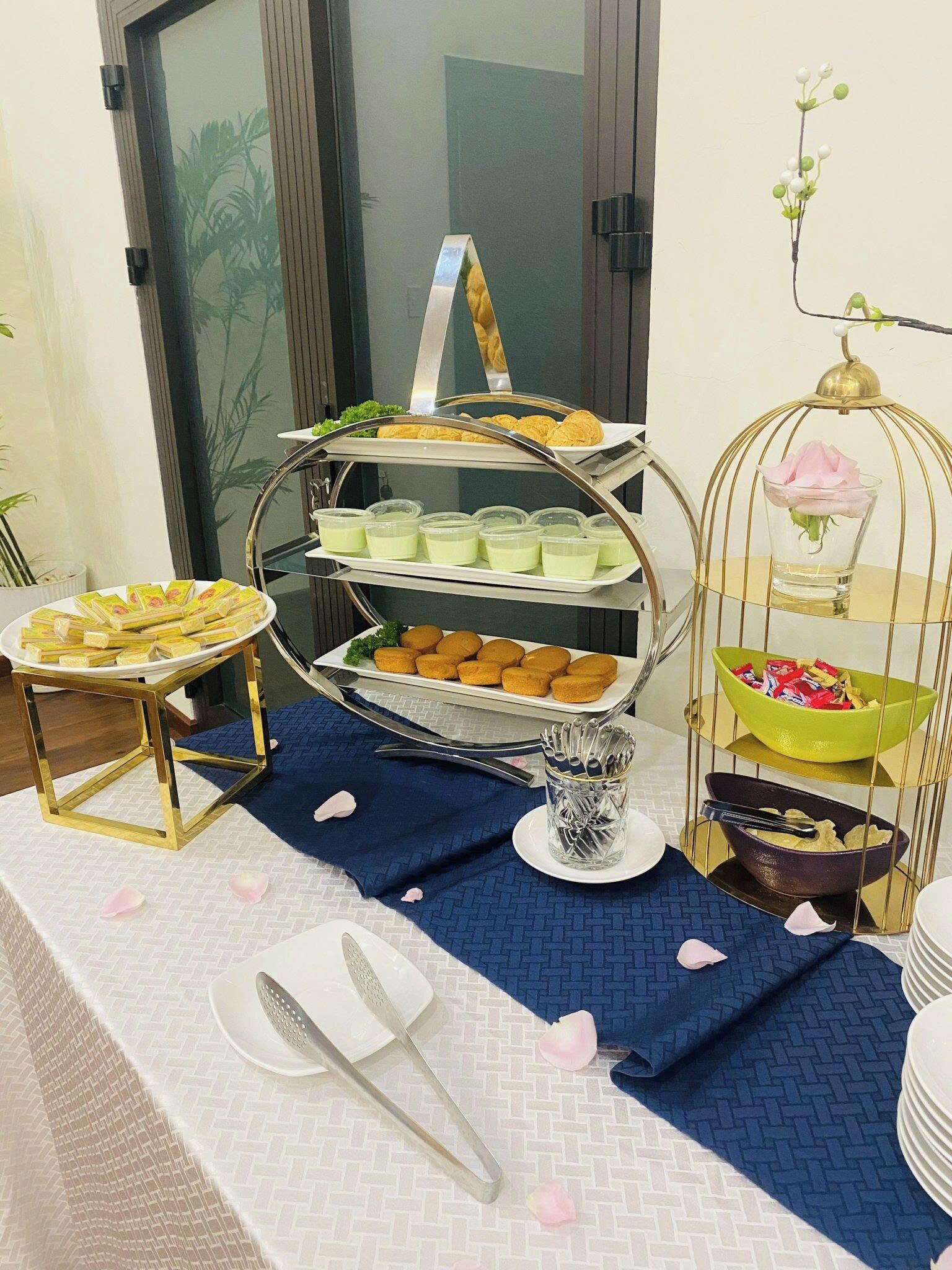 A buffet setup with multiple trays of food, including pastries and desserts, arranged on a table with a blue cloth.