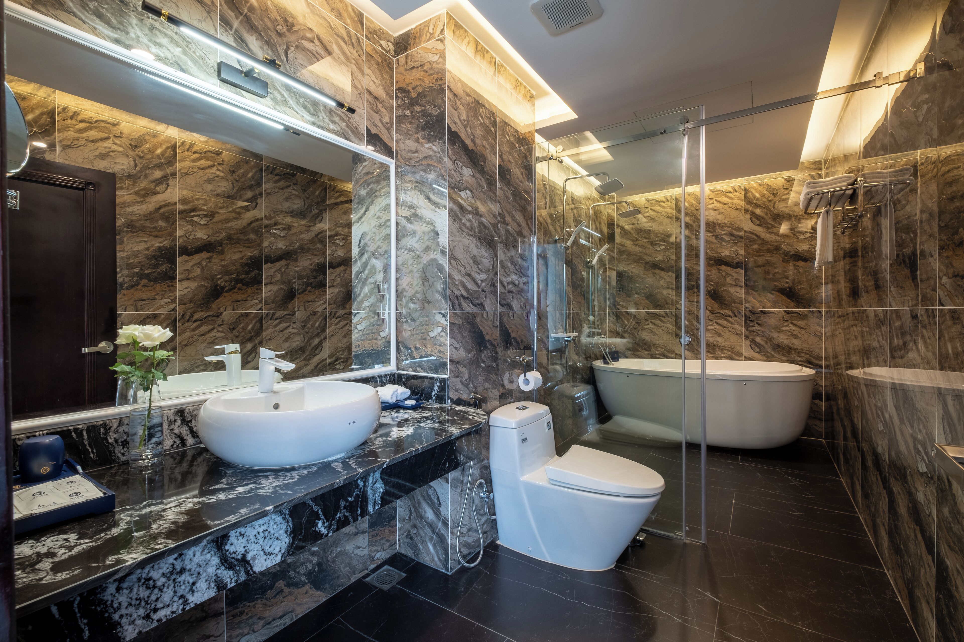 Ein modernes Badezimmer mit Marmorwand, Waschbecken in Weiß, Toilette und freistehender Badewanne.