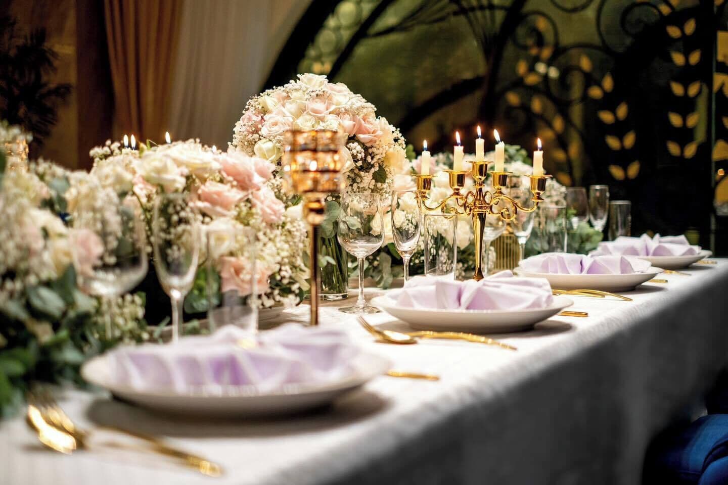 A table set with white plates, gold cutlery, and a candelabra with lit candles.