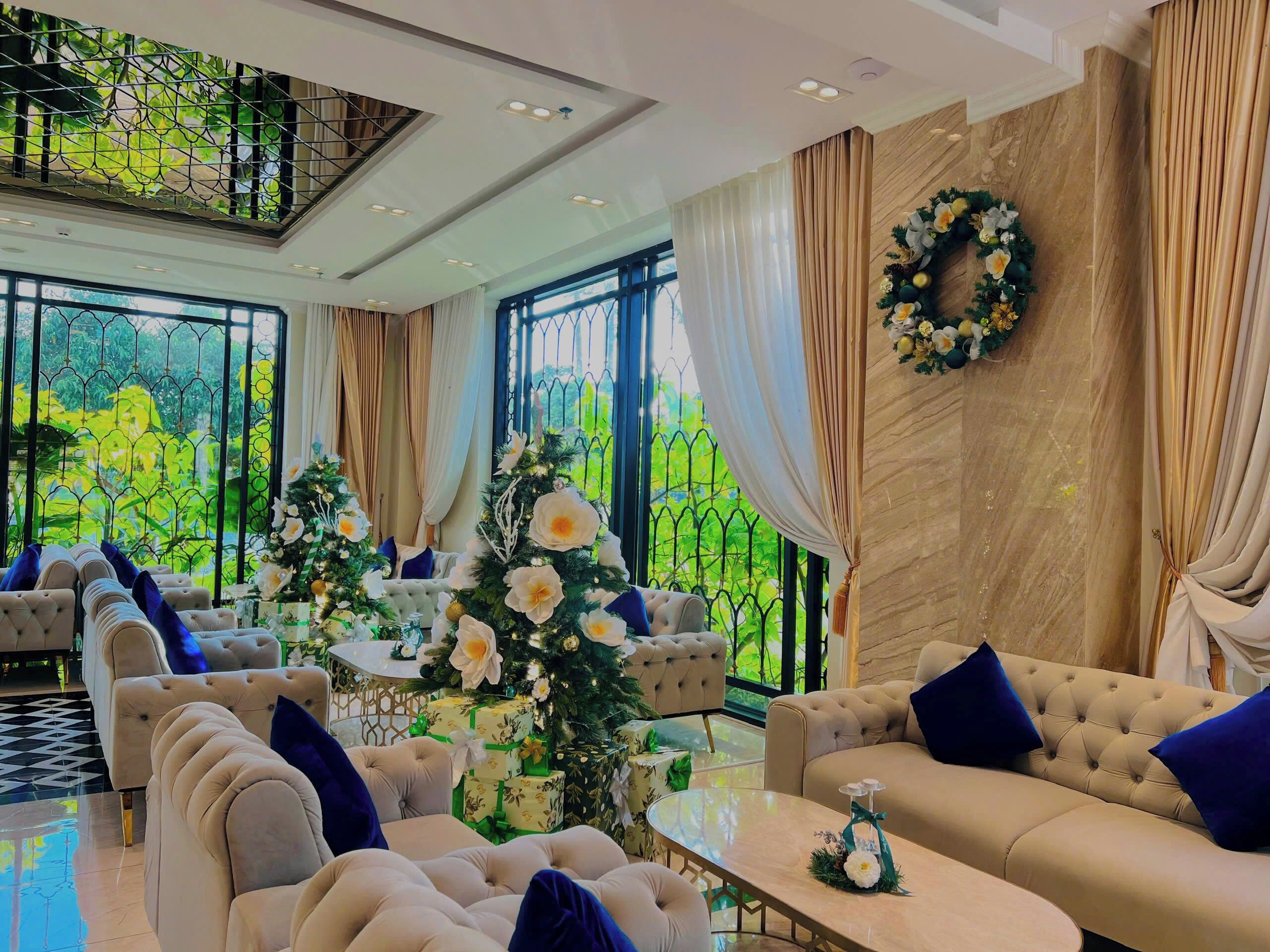 Ein geräumiger Raum mit hoher Decke, großen Fenstern und Blick auf die grüne Umgebung. Zwei Sofas und ein Couchtisch, dazu ein Weihnachtsbaum und Blumenarrangements.