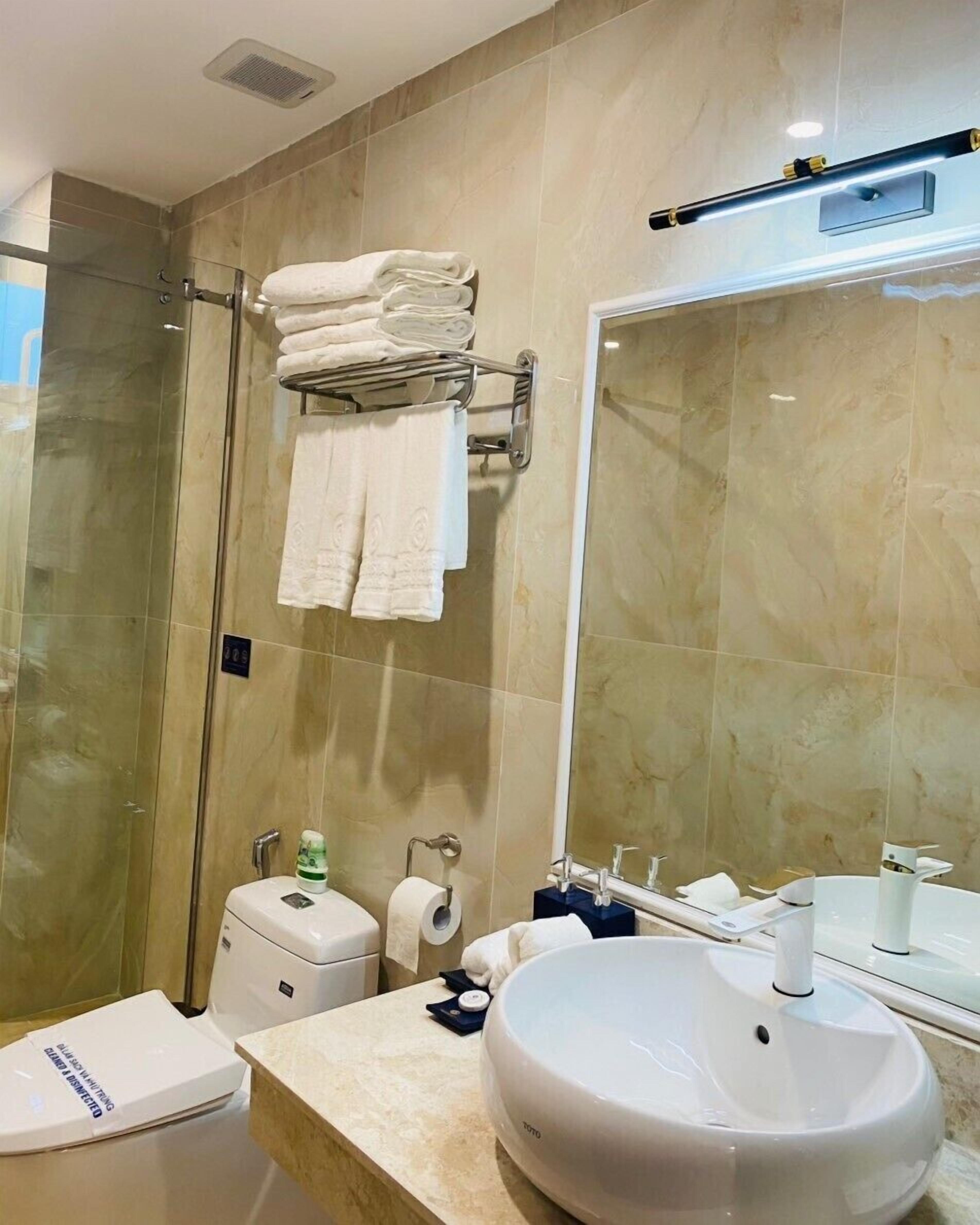 A modern bathroom with a glass shower enclosure, a large mirror, a white sink, and neatly folded towels on a rack.