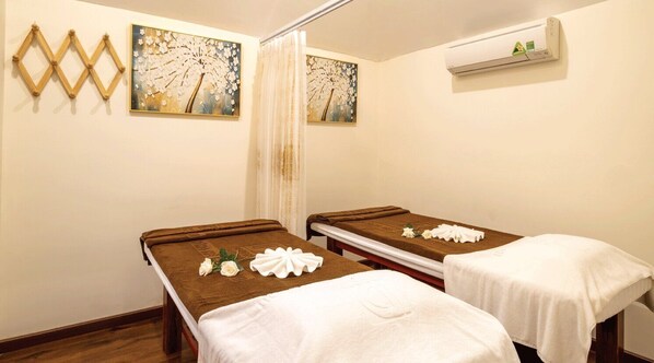 A room with two massage tables, each with a towel and a flower arrangement. There are wall-mounted air conditioning units and artwork above the tables. - Sandals Vista (1 Bao Loc)