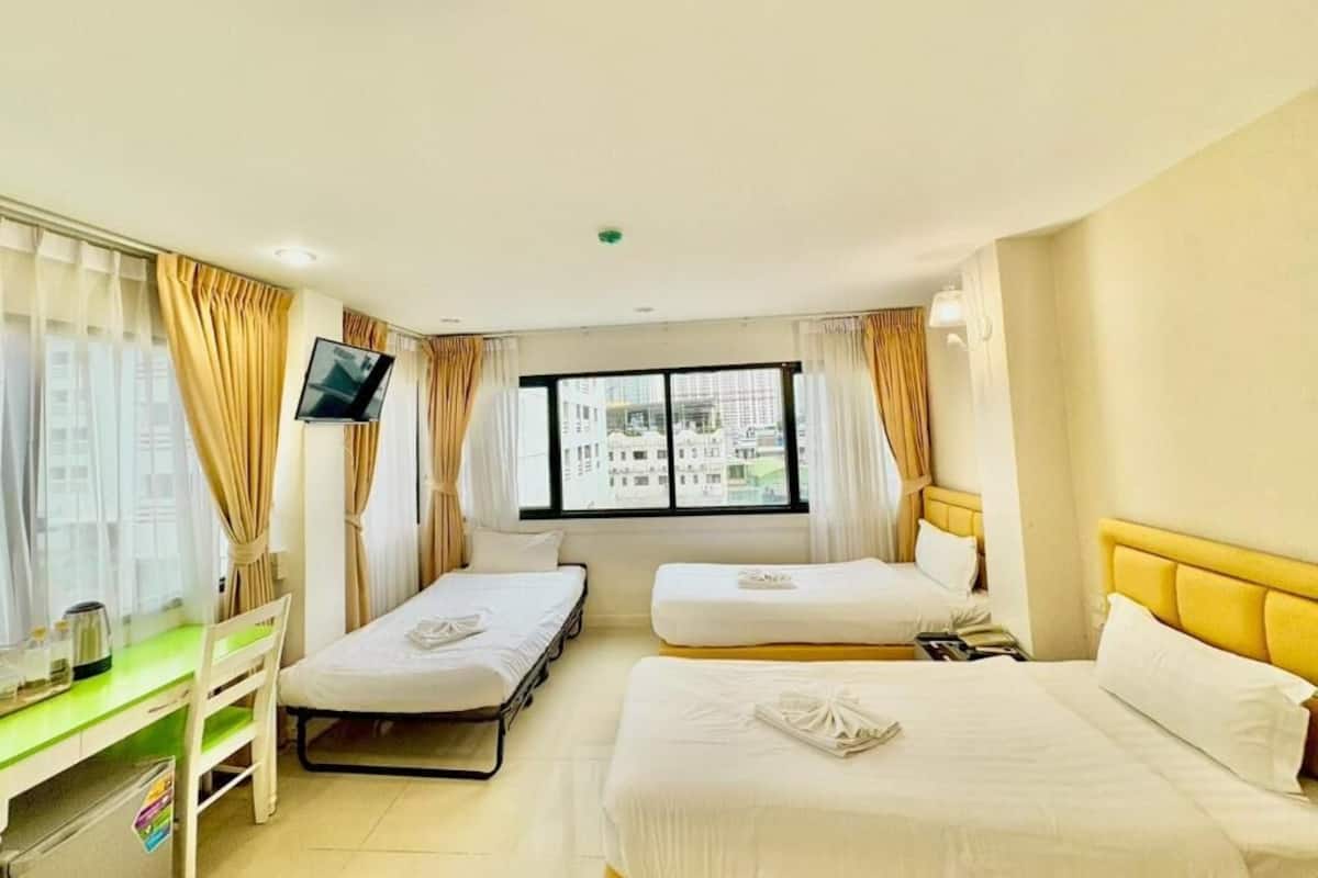 A hotel room with two beds, a desk, a TV, and a window with a city view.