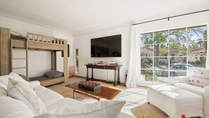 A modern living room with a bunk bed, a flat-screen TV, a coffee table, and a large window offering a view of the street. - Enjoy indoor-outdoor living, full kitchens and walk to beach and state st. (Santa Barbara)