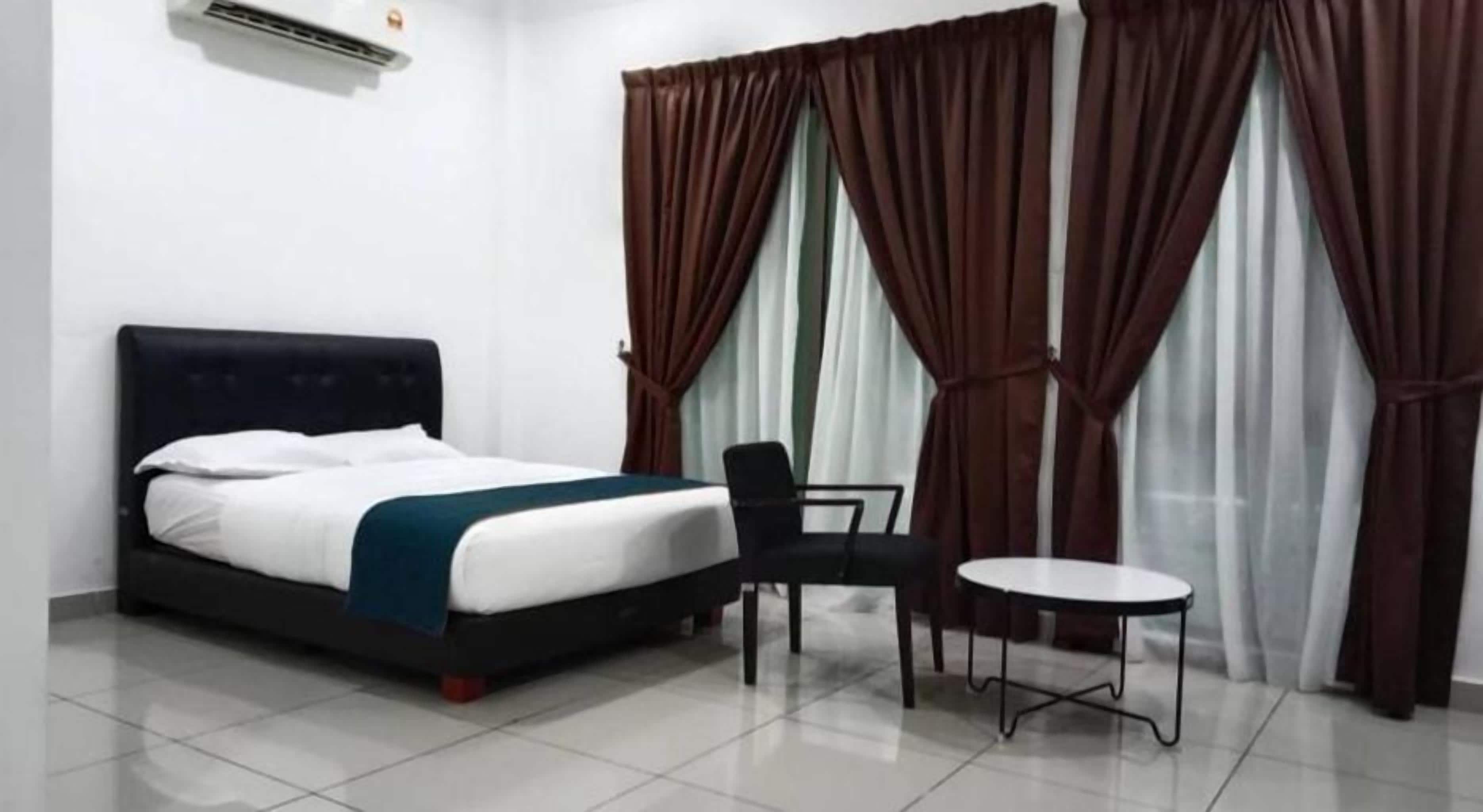 A hotel room with a bed, a chair, a small table, and curtains.