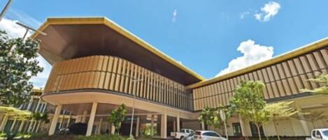 A modern building with a curved facade, a covered entrance, and a parking area with cars.