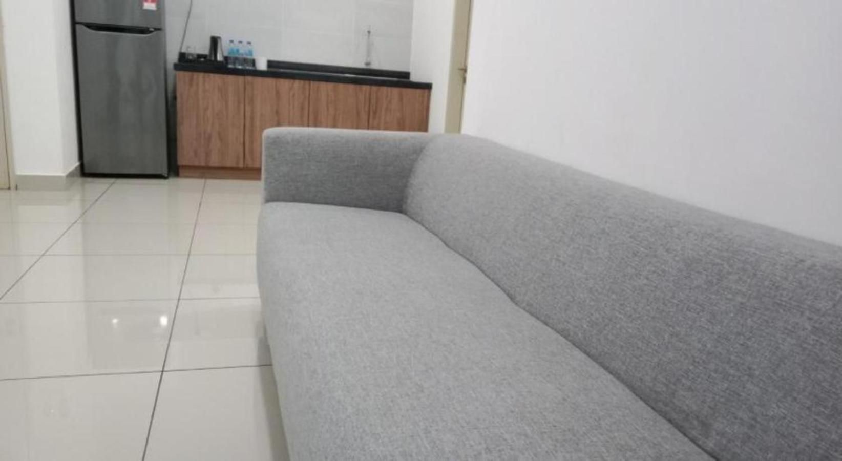 Un sofá gris en una habitación con suelo de baldosas y una zona de cocina al fondo.