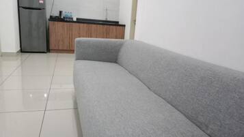 Un sofá gris en una habitación con suelo de baldosas y una zona de cocina al fondo.