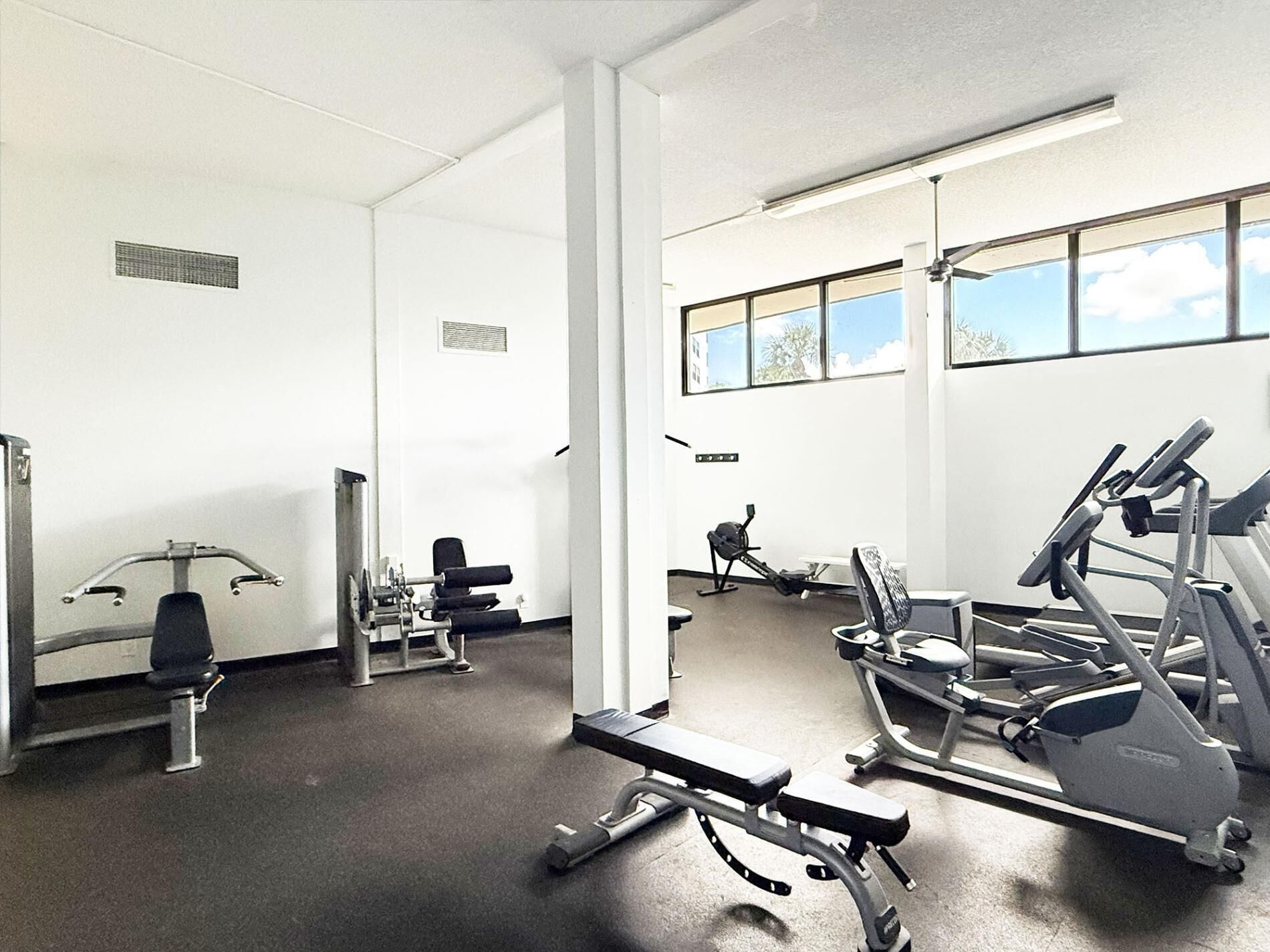 Een sportschool met diverse trainingsapparaten, waaronder loopbanden en gewichtstoestellen, met grote ramen voor veel daglicht.