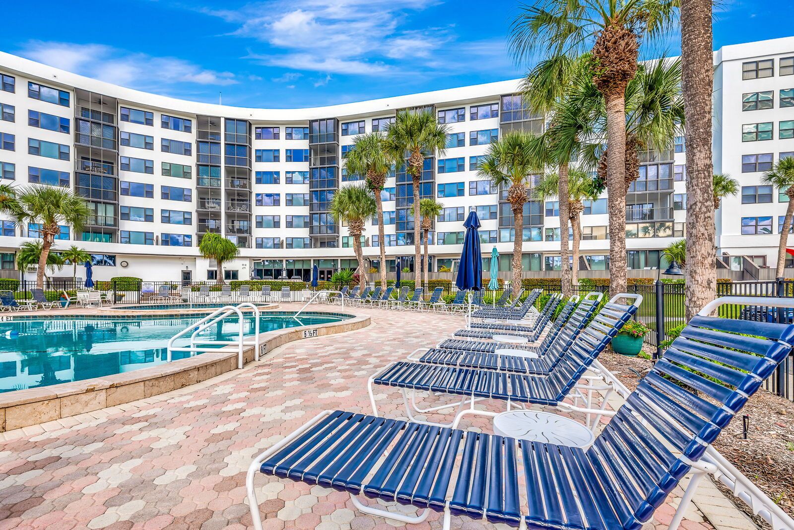 A hotel pool area with a curved pool, lounge chairs, and palm trees.