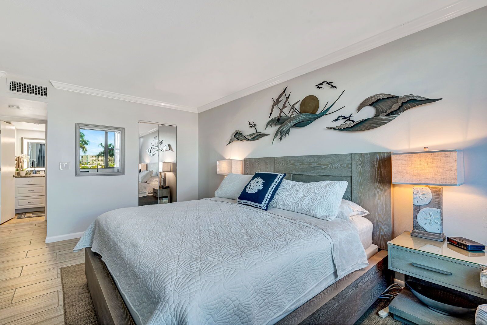 A bedroom with a large bed, a nightstand, a lamp, and a wall art piece.