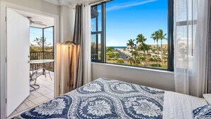 Une chambre dotée d’une grande fenêtre donnant sur la côte, d’un lit recouvert d’une couvre-lit à motifs et d’un balcon avec une table et des chaises.