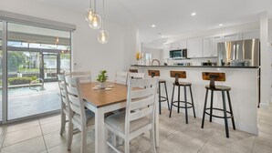 A modern kitchen with white cabinets, a stainless steel refrigerator, and a dining area with a wooden table and white chairs. - 3BR Waterfront Home – Heated Saltwater Pool & Dock (Punta Gorda)