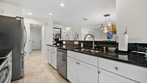 A modern kitchen with white cabinetry, a black granite countertop, and stainless steel appliances. - 3BR Waterfront Home – Heated Saltwater Pool & Dock (Punta Gorda)