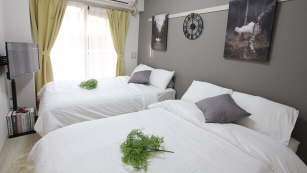 Quarto de hotel com duas camas, uma televisão de tela plana, um relógio de parede e uma janela com cortinas.