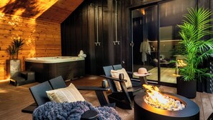 A modern outdoor seating area with a fire feature, wooden flooring, and a hot tub.