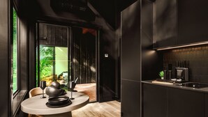A modern kitchen with dark cabinetry, a round dining table, and a view of a lush garden through a glass door.